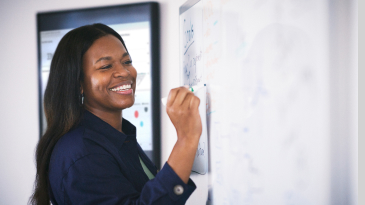 A smiling person writing on a whiteboard