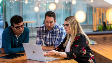 Three people hovering over a laptop screen 