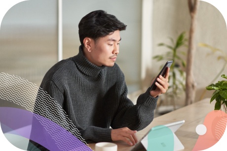 A person at a table uses a handheld device and a tablet