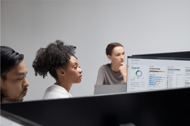 Three people in a conference room with a screen showing charts