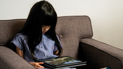 A girl is watching a tablet on an armchair