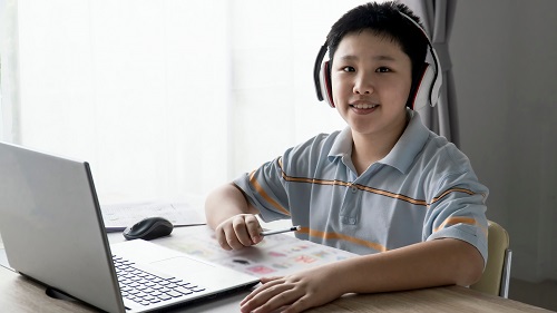 A boy is wearing a headphone in front of a laptop