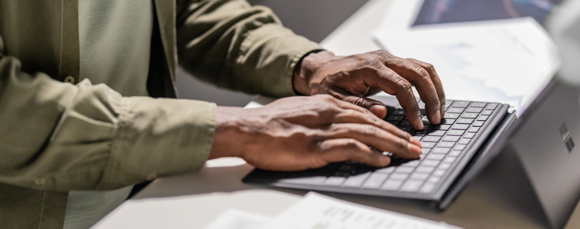 Close-up of hands typing on a laptop keyboard with documents nearby.