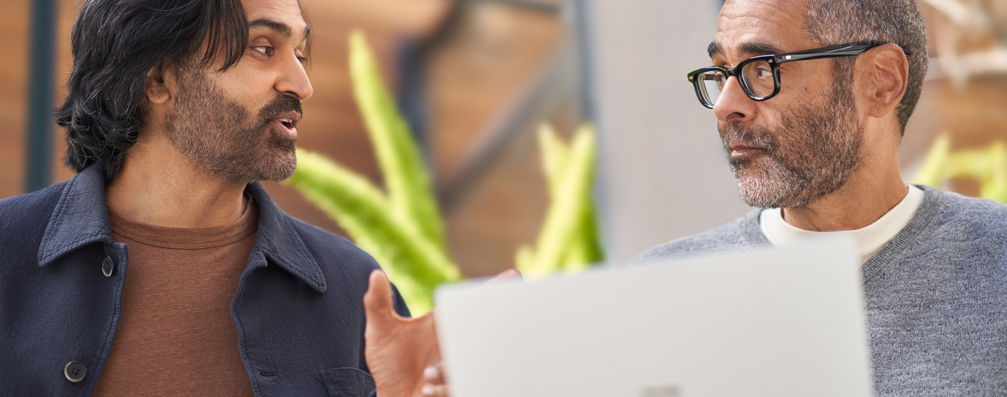 two men conversing with a laptop in front of them