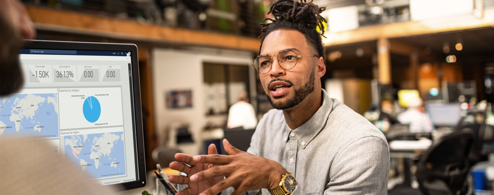 Person discussing data insights displayed on a monitor showing analytics charts and global activity maps in a modern office.