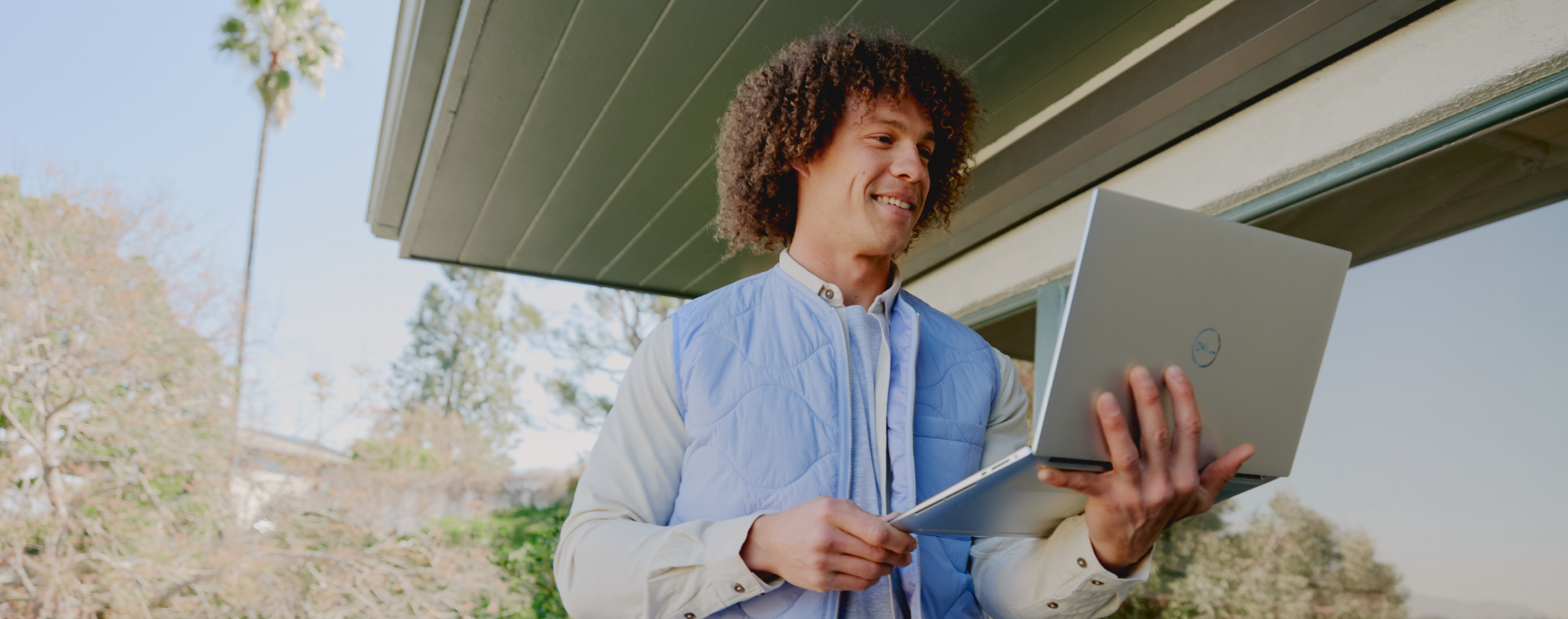 Man smiling as he walks outside holding a laptop