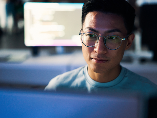 A person viewing a computer screen with code appearing on a screen in the background.