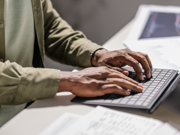 Close-up of hands typing on a laptop keyboard with documents nearby.