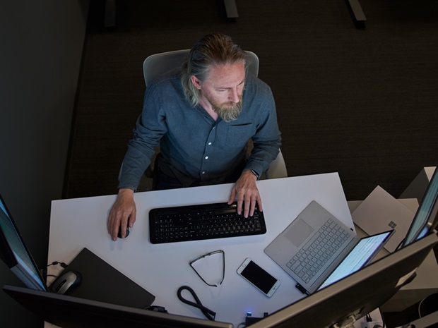 Overhead view of man typing at a workstation with multiple monitors