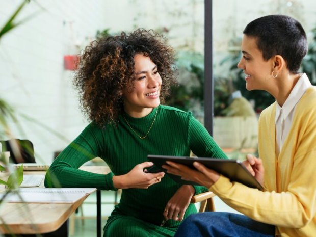 Two people having a conversation while holding a tablet.
