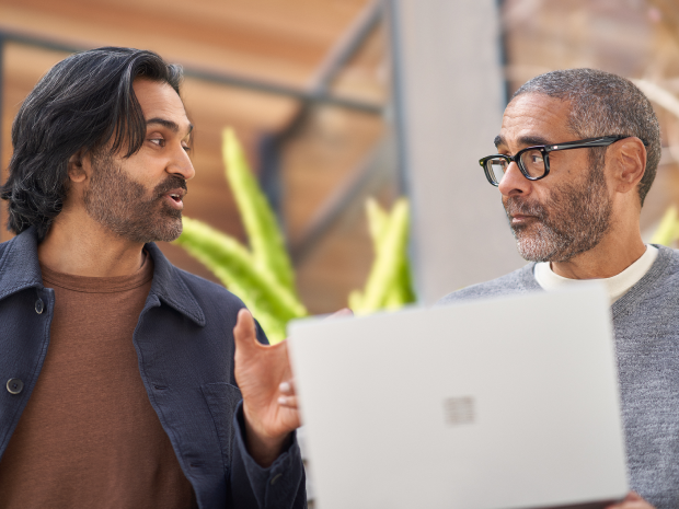 two men conversing with a laptop in front of them