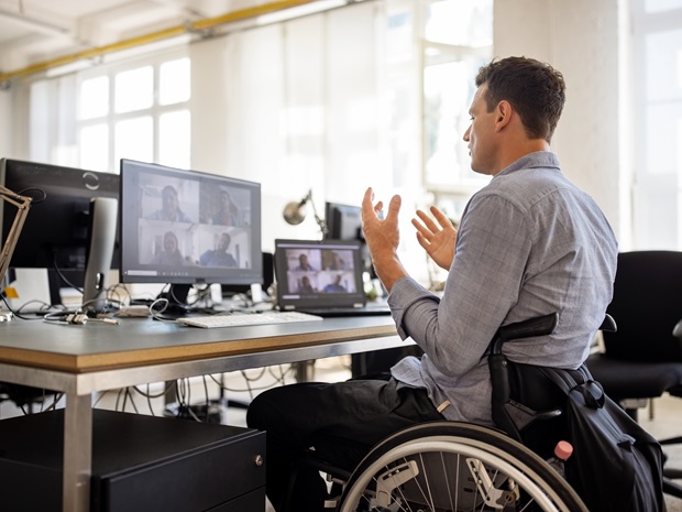 A businessman in a wheelchair speaks to his team during a video conference call on his computer.