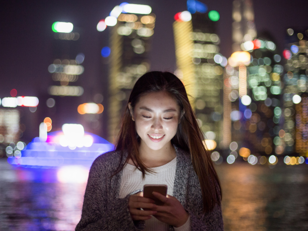 A person looks at their mobile device in an Asian city at night