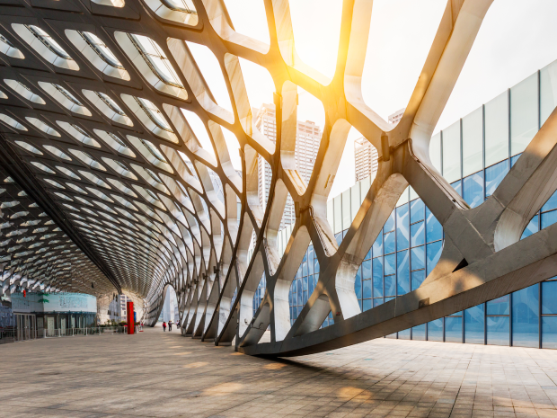A modern architectural structure with a geometric metal lattice and glass facade illuminated by sunlight, symbolizing innovation and technology.
