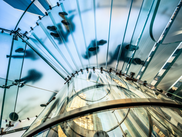 A view from below of people walking on a modern glass spiral staircase in a city building.