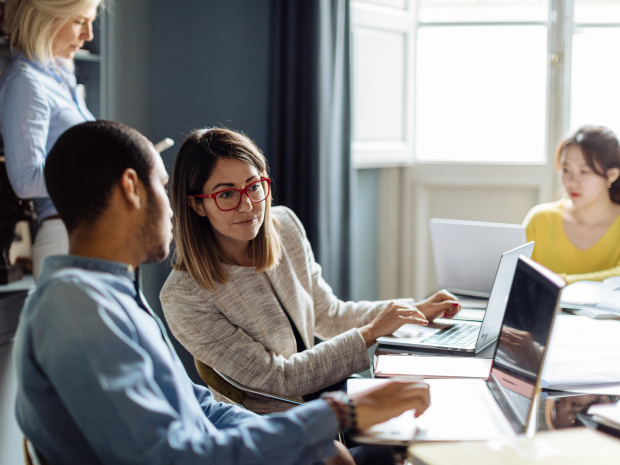 Two people at a conference room table looking at a laptop screen together.