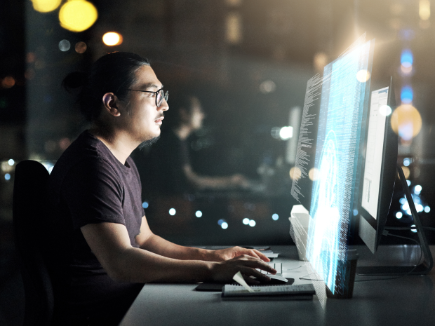Person working at a computer with code on the screen, city lights in the background.