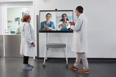 Two healthcare workers speaking with others on a big screen