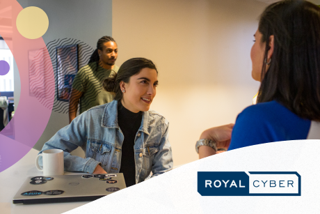 Two people talking in an office setting as another walks by.