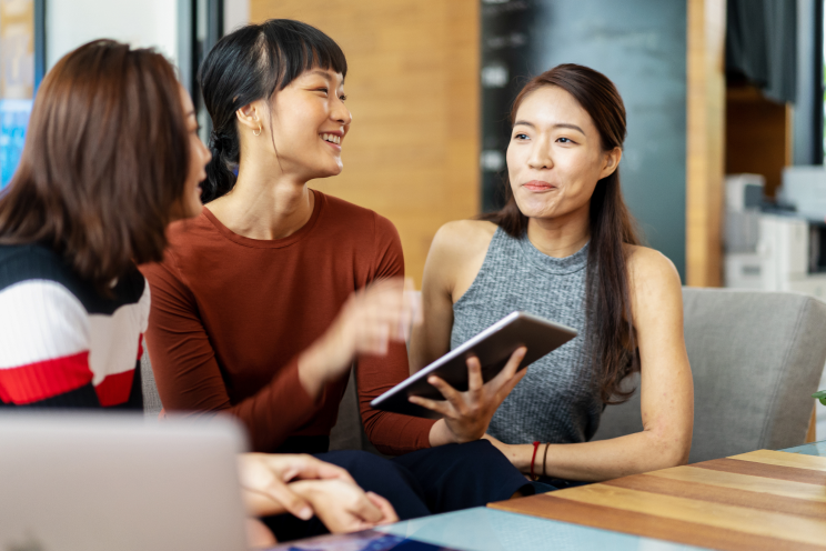 Three people talking over a tablet.
