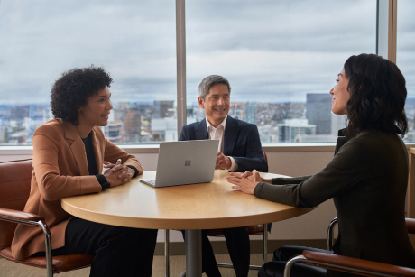 Three colleagues have a conversation around a table with an open laptop on it