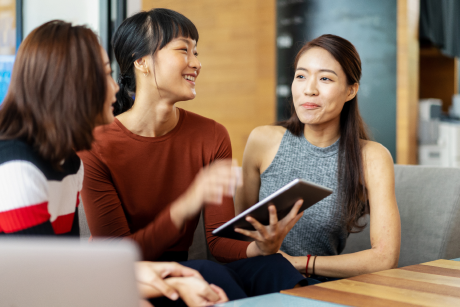Three people talking over a tablet.