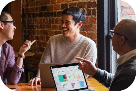 Three people laughing at a table with laptops.