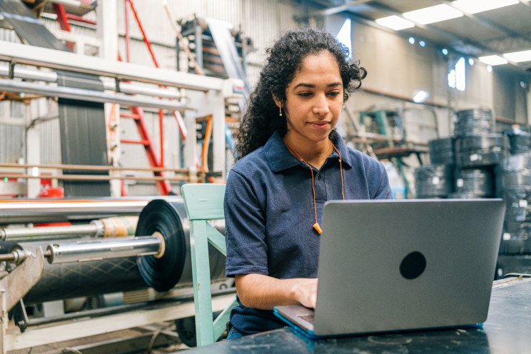 A person using a laptop at a desk in a factory