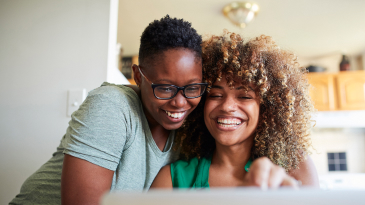 Two people smiling looking at computer monitor together