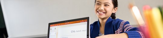 Child smiling and sitting in front of a laptop