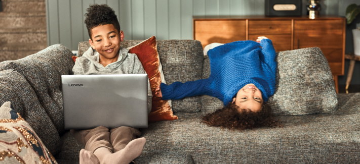 Two kids on a couch laying down and using a laptop