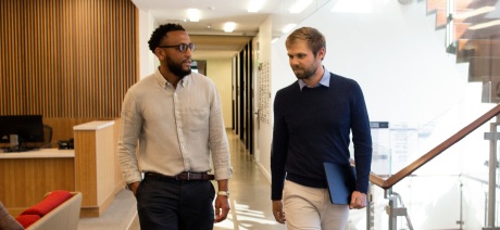 Two Men walking along a hallway having a discussion