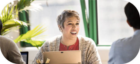 A person holding a tablet and smiling while speaking to others in an office