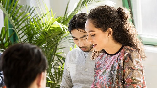 Woman and man smiling near a plant while looking down